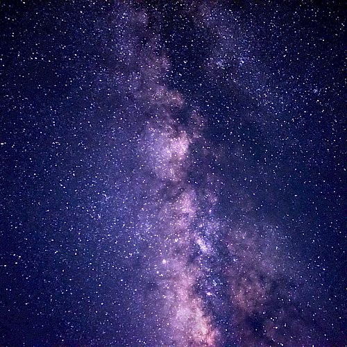 A vibrant night sky with the Milky Way galaxy visible, showcasing numerous stars against a dark, purple-toned backdrop.