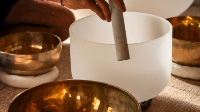 A hand is playing crystal and brass singing bowls, often used for meditation and sound healing practices.
