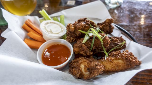 A plate of fried chicken wings with sliced green onions, accompanied by carrot sticks, celery, ranch, and hot sauce, served with a drink.
