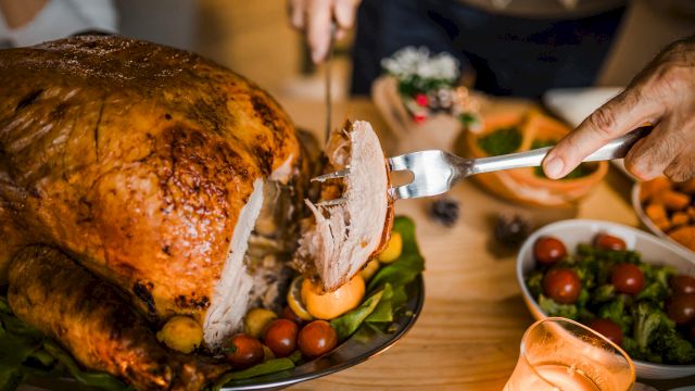 A person carves a roasted turkey on a table set with various dishes, including salads and sides, under warm candlelight.